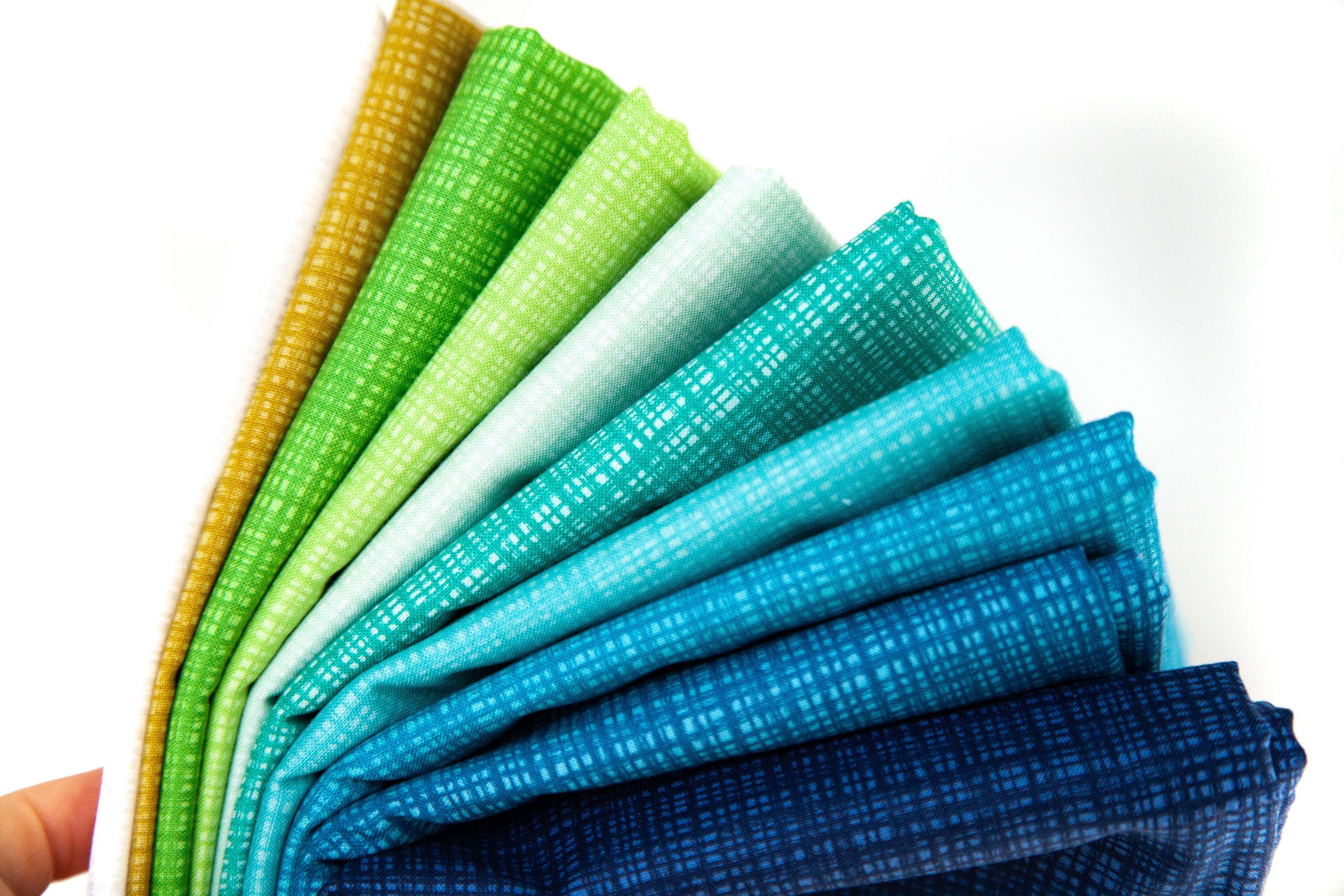 Set of folded fabric swatches in green, blue, and yellow on a white background