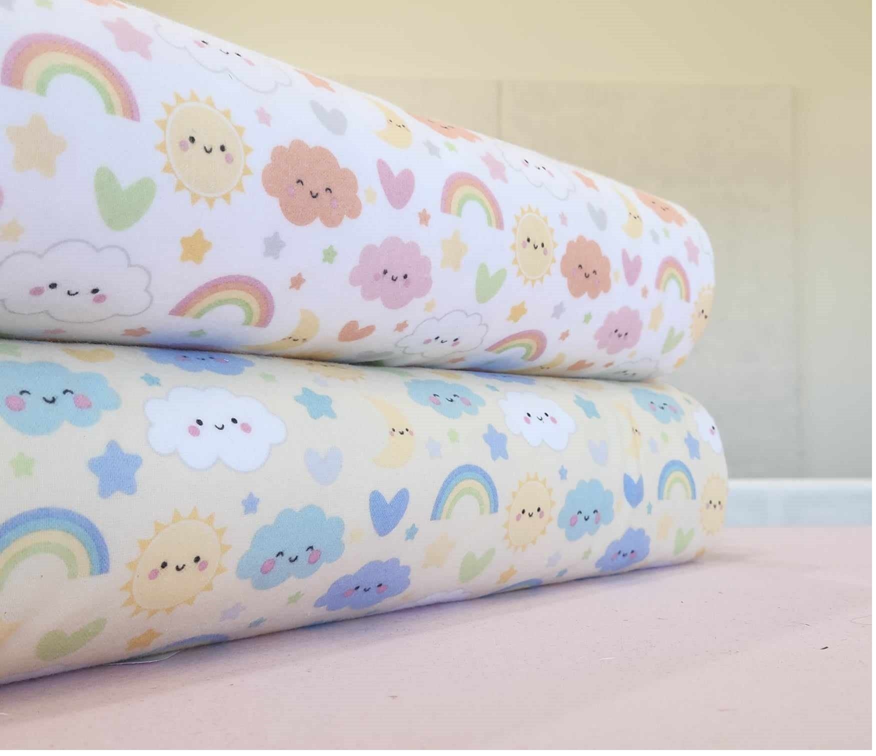 Two rolls of fabric with colorful patterns of clouds, suns, and rainbows on a light background.